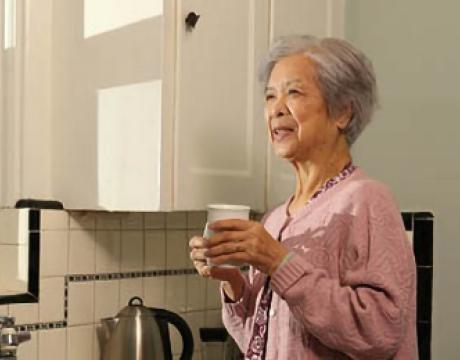 Image of a smiling senior woman standing in her kitchen holding a cup